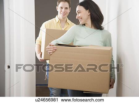 Stock Image - Couple carrying boxes in new house. Fotosearch