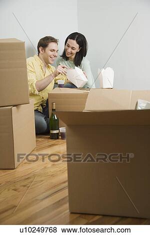 Stock Photo - Couple eating take out on boxes in new house. Fotosearch