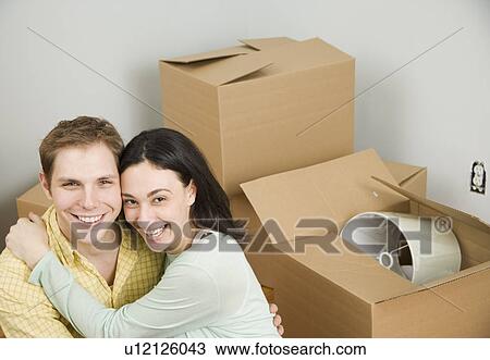 Stock Image - Couple hugging next to boxes in new house. Fotosearch