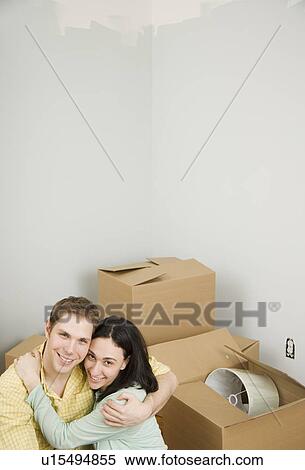 Stock Photography - Couple hugging next to boxes in new house. Fotosearch