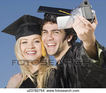 Couple in graduation caps and gowns video recording selves View Large Photo Image Picture - Couple in graduation caps and gowns video recording selves. Fotosearch