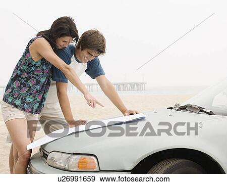 Stock Photo - Couple looking at map on car hood at beach. Fotosearch