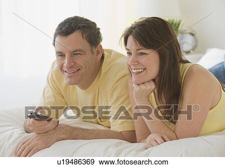 Couple pointing remote control on bed View Large Photo Image Stock Photo - Couple pointing remote control on bed. Fotosearch