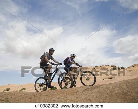 Stock Image - Couple riding mountain bikes in desert. Fotosearch