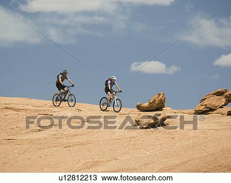 Stock Image - Couple riding mountain bikes in desert. Fotosearch