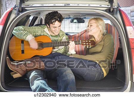 Stock Image - Couple sitting in back of car with guitar. Fotosearch