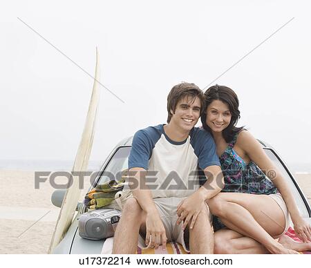 Picture - Couple sitting on hood of car at beach. Fotosearch