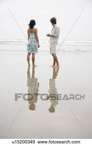 Couple standing on beach looking at waves View Large Photo Image Stock Photo - Couple standing on beach looking at waves. Fotosearch