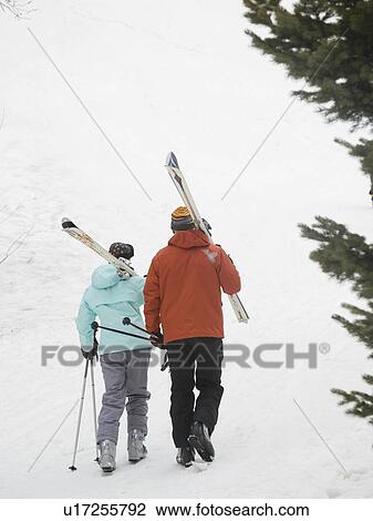 Stock Image - Couple walking with skis over shoulders. Fotosearch