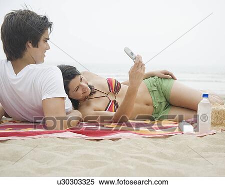 Couple with cell phone on blanket at beach View Large Photo Image Stock Photography - Couple with cell phone on blanket at beach. Fotosearch