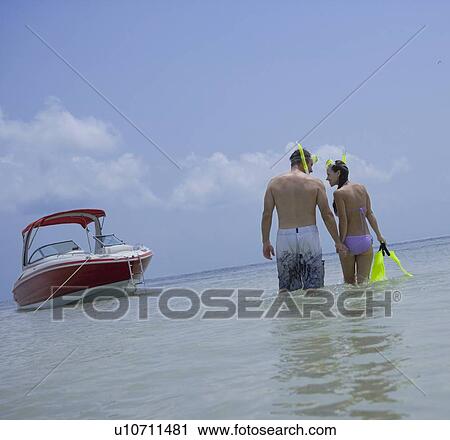Stock Image - Couple with snorkeling gear walking in water, Florida, United States. Fotosearch