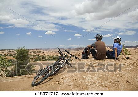Cyclists sitting next to mountain bikes in desert View Large Photo Image Stock Photo - Cyclists sitting next to mountain bikes in desert. Fotosearch