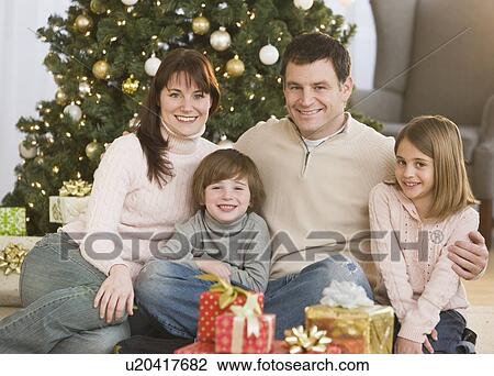Stock Image - Family hugging in front of Christmas tree. Fotosearch