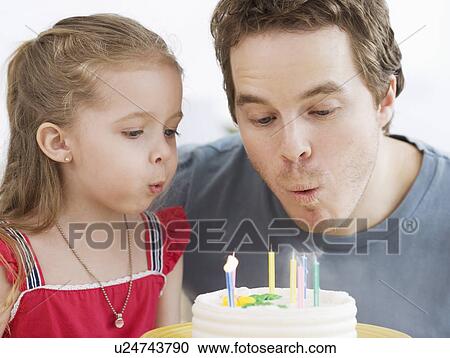 Stock Image - Father and daughter blowing out birthday candles. Fotosearch