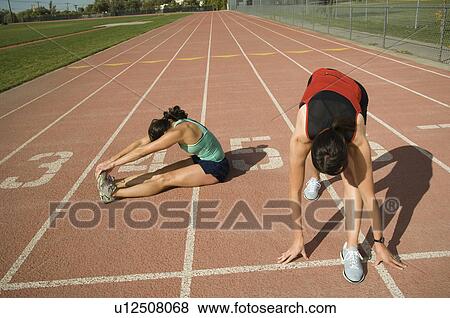 Stock Photo - Female runners stretching on track, Utah, United States. Fotosearch