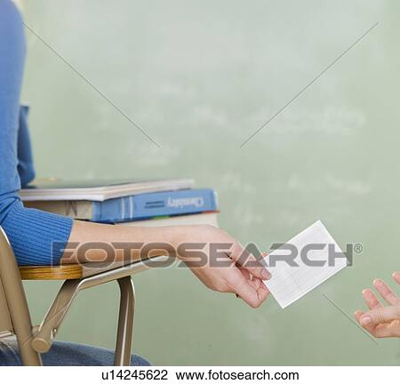 Stock Image - Female student passing a note in class. Fotosearch