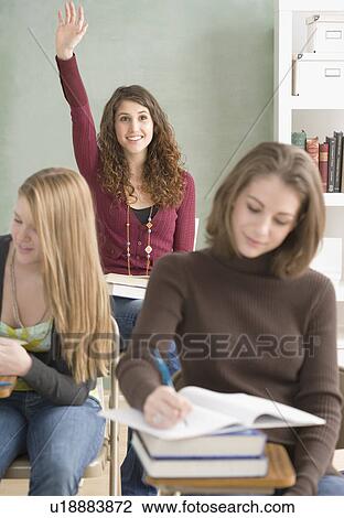 Stock Image - Female student raising hand in classroom. Fotosearch