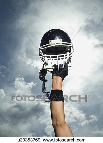 Stock Photo - Football player holding helmet in air. Fotosearch