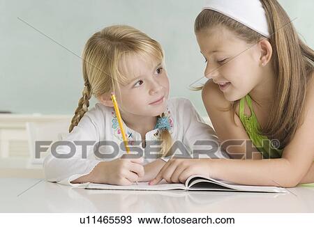 Stock Image - Girl helping classmate at desk. Fotosearch
