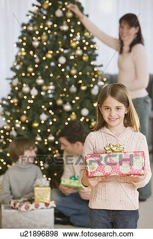 Stock Photo - Girl holding Christmas gift in front of family. Fotosearch
