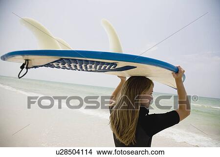 Picture - Girl holding surfboard on head, Florida, United States. Fotosearch