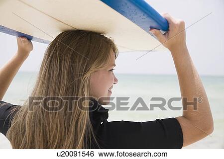 Stock Photograph - Girl holding surfboard on head, Florida, United States. Fotosearch