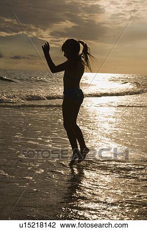 Stock Image - Girl in ocean surf at sunset, Florida, United States. Fotosearch
