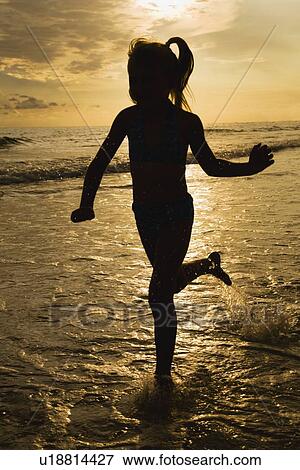 Stock Photo - Girl running in ocean surf at sunset, Florida, United States. Fotosearch