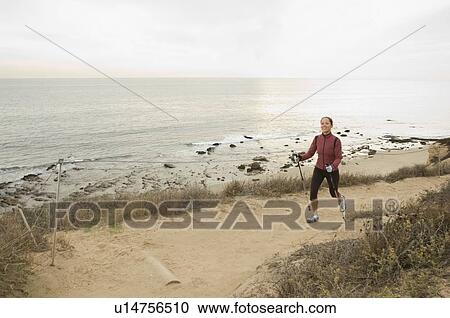 Stock Image - Hispanic woman pole walking along coast in California, United States. Fotosearch