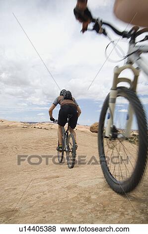 Stock Photo - Low angle view of couple riding mountain bikes. Fotosearch