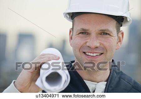 Stock Image - Male construction worker holding blueprints. Fotosearch