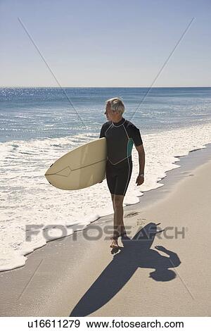 Stock Photo - Man carrying surfboard at beach. Fotosearch