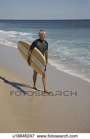 Stock Photo - Man carrying surfboard at beach. Fotosearch