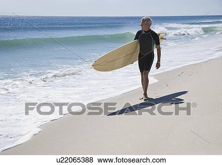 Man carrying surfboard at beach View Large Photo Image Stock Photo - Man carrying surfboard at beach. Fotosearch