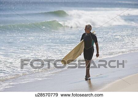 Stock Photo - Man carrying surfboard at beach. Fotosearch