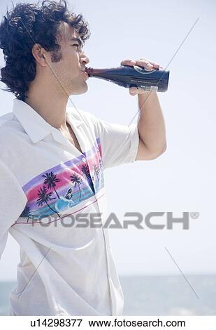 Stock Photo - Man drinking bottle at beach. Fotosearch