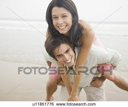 Stock Photograph - Man giving woman piggyback ride at beach. Fotosearch