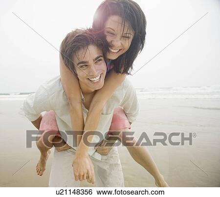 Stock Photograph - Man giving woman piggyback ride at beach. Fotosearch