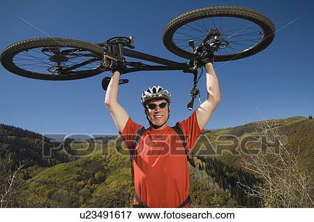 Stock Photo - Man holding mountain bike over head, Utah, United States. Fotosearch