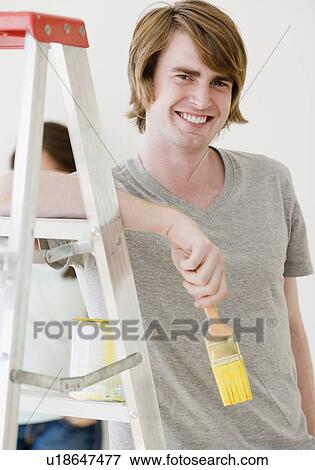 Stock Photo - Man holding paintbrush next to ladder. Fotosearch