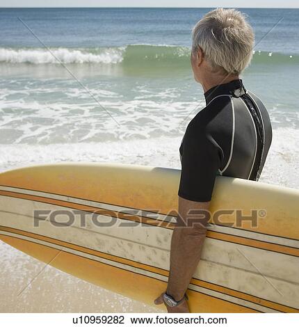 Man holding surfboard at beach View Large Photo Image Stock Image - Man holding surfboard at beach. Fotosearch