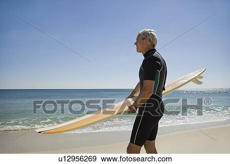 Man holding surfboard at beach View Large Photo Image Stock Photo - Man holding surfboard at beach. Fotosearch