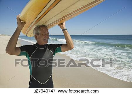 Stock Photo - Man holding surfboard at beach. Fotosearch