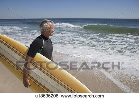 Man holding surfboard at beach View Large Photo Image Stock Photograph - Man holding surfboard at beach. Fotosearch