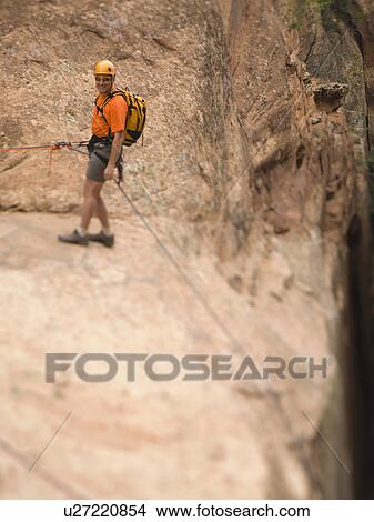 Picture - Man in rappelling gear at top of cliff. Fotosearch