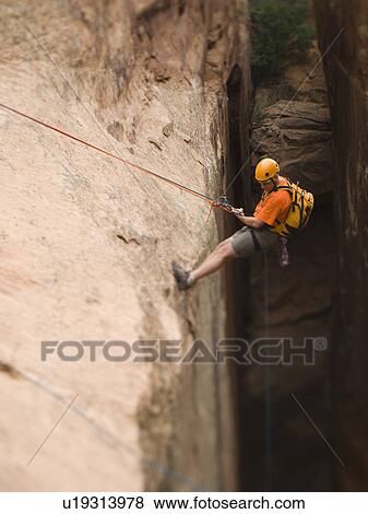 Stock Photo - Man in rappelling gear at top of cliff. Fotosearch