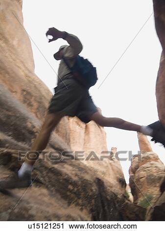 Stock Image - Man jumping over rock formations. Fotosearch