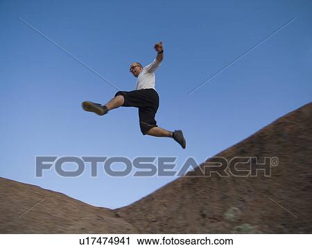 Stock Image - Man jumping over rock formations. Fotosearch