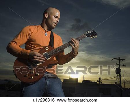 Stock Photograph - Man playing guitar at dusk. Fotosearch