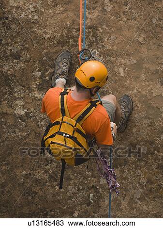 Stock Image - Man rappeling down cliff. Fotosearch